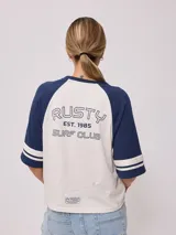 Remera bicolor Rusty de corte holgado y estilo deportivo, con cuerpo blanco y mangas raglán azules con doble raya blanca. Presenta estampado frontal con el texto 'RUSTY 85'.