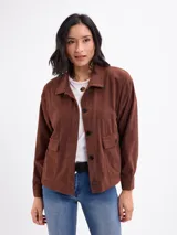 Campera de pana color beige, con cuello camisero, cierre frontal de botones oscuros, mangas largas con puños abotonados y dos bolsillos frontales con solapa.