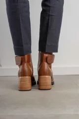 Bota corta de cuero negro con acabado combinado mate y charol. Presenta una tira decorativa con tachas metálicas y hebilla en el tobillo, tacón cuadrado robusto y suela con plataforma.