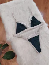 Conjunto de lencería compuesto por bralette triangular y tanga, confeccionado en algodón color verde inglés con detalles de encaje en tono nude. El bralette cuenta con breteles ajustables y broche regulable, mientras que la tanga presenta laterales ajustables.