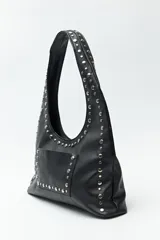 Cartera tipo hobo de símil cuero texturizado color marrón oscuro, con apliques de tachas metálicas plateadas que recorren el frente y el contorno. Cuenta con un bolsillo frontal y un asa de hombro.