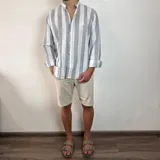 Camisa de manga larga con cuello mao, confeccionada en tejido de lino a rayas verticales en tonos blanco y celeste. Presenta cierre frontal con botones y corte clásico.