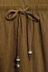 Pantalón de tiro medio y pernera recta con textura, de color marrón. Cuenta con cintura elástica y cordón ajustable con abalorios decorativos.