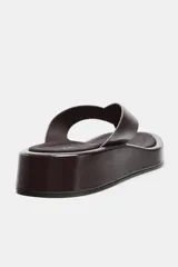 Sandalia plana color marrón con tira delantera para el dedo y suela con plataforma.