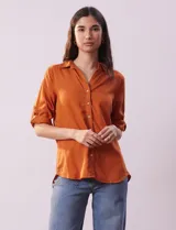 Camisa color beige de tencel, marca Hester & Orchand, con cuello con solapa, escote en V, abertura central con botones y bolsillos delanteros. Las mangas son largas y regulables con presilla y botón.