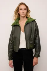 Chaqueta estilo bomber de cuero vacuno en color verde vintage, con cuello y forro interior de corderito al tono. Presenta cierre frontal completo y un diseño de inspiración retro con acabado texturizado.
