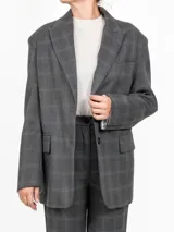 Blazer gris a cuadros con dos botones frontales y bolsillos laterales. Las mangas interiores blancas se pueden doblar para un toque distintivo.