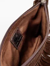 Sobre de mano confeccionado en gamuza marrón, con diseño de flecos colgantes, franja de cuero texturizado, cierre superior y correa de muñeca desmontable.
