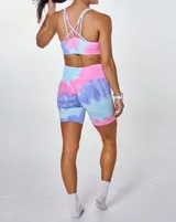 Conjunto deportivo de dos piezas compuesto por un top deportivo de escote redondo y un short ciclista de tiro alto. Ambas prendas presentan un diseño estampado con efecto tie-dye en tonos azul, rosa y violeta.