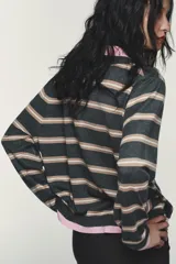 Jersey de punto a rayas horizontales en tonos gris, beige y blanco, con cuello polo y puños en color rosado. Presenta cierre frontal con botones y diseño de manga larga.