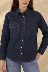 Camisa de jean de corte clásico estilo western, confeccionada en denim liviano de color azul oscuro. Presenta bolsillos frontales con solapa, costuras pespunteadas en contraste y cierre frontal con broches metálicos a presión.