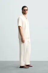 Camisa de corte regular fit confeccionada en tejido con estructura de color negro. Cuenta con cuello bowling, manga corta, aberturas laterales en el bajo y cierre frontal de botones.