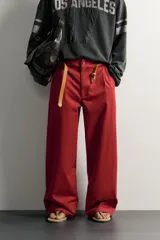 Pantalón wide fit color rojo terracota, con pliegues frontales, bolsillos laterales y cierre frontal con cremallera y botón.