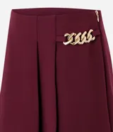 Short pollera de sastrería marca Cortelle, color bordó, confeccionado en crepé. Presenta sobreposición frontal efecto pollera con pliegues y detalle de cadena metálica decorativa en el lateral.
