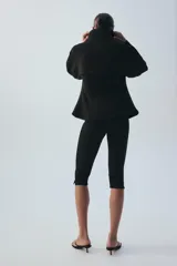 Chaqueta negra de manga larga con cuello subido, bolsillos delanteros y cierre frontal con botones ocultos bajo solapa.