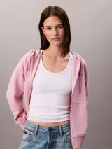 Buzo con capucha de Calvin Klein, de corte cropped y color rosado, confeccionado en mezcla de algodón y poliéster. Cuenta con cierre frontal de cremallera, cordones ajustables en la capucha y bolsillos tipo canguro. Presenta el logo de la marca bordado discretamente en el pecho.