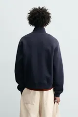 Sudadera de corte relajado confeccionada en tejido de algodón. Presenta cuello subido con cierre frontal de cremallera metálica, manga larga y acabados en rib en puños y bajo.