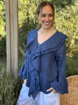 Camisa de lino azul marino con volados en cascada a lo largo del frente y en los puños de las mangas largas. Presenta un escote en V con un botón de nácar visible.