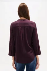 Blusa de viscosa color bordó, con cuello en V, cierre frontal parcial con botones, mangas tres cuartos y bolsillo aplicado en el pecho.
