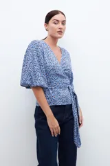 Blusa cruzada celeste con estampado floral, mangas cortas abullonadas y lazo en la cintura.