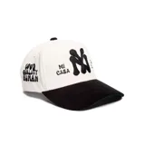 Gorro tipo cap de pana, color blanco con visera negra. Cuenta con el logotipo NY bordado en relieve en el centro y las frases "Mi Casa" y "Su Casa" bordadas a los lados.