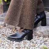 Bota corta de cuero negro con diseño combinado, presentando una textura lisa en la parte frontal y una textura tipo reptil en el talón. Cuenta con taco cuadrado alto, plataforma delantera y cierre lateral interno.