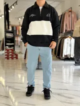 Buzo de algodón negro con una franja horizontal blanca en el centro, cuello solapa con medio cierre y puños y cintura elásticos acanalados. Cuenta con pequeños estampados en el pecho.