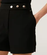 Short negro de sastrería con cintura alta, bolsillos laterales y cierre frontal con botones dorados.