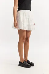 Falda corta blanca con volados en capas, confeccionada en tejido de algodón con bordado estilo broderie. Cuenta con cintura elástica.