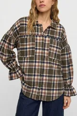 Camisa de manga larga con estampado de cuadros en tonos verde, beige y azul. Presenta cuello clásico, cierre frontal con botones, dos bolsillos delanteros y mangas con puños elásticos y detalle de volado.