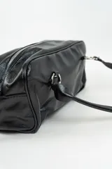 Bolso de mano tipo bowling de cuero sintético negro, con diseño estructurado, costuras decorativas y detalles de tiras largas en los laterales. Cuenta con asas cortas trenzadas con argollas metálicas.