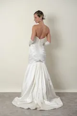 Vestido de novia largo color marfil, confeccionado en piel de ángel drapeada. Diseño strapless con apliques bordados en piedras en el escote, la cintura y la cola. Incluye guantes largos de satén blanco.