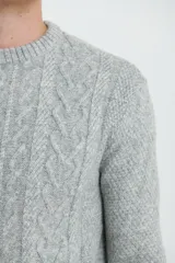 Sweater de tejido de punto color beige claro, con diseño de trenzas (aranes) en el frente y mangas de punto liso. Tiene cuello redondo.