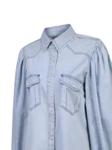 Blusa de jean celeste claro con mangas largas abullonadas, cuello camisero, bolsillos frontales con tapeta y cierre de broches metálicos a presión.