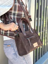 Cartera bandolera de cuero color marrón chocolate, con forro de tela y herrajes dorados. Tiene doble asa de mano y correa larga regulable y desmontable. Incluye bolsillo frontal con cierre y bolsillo interno.