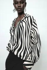 Camisa de manga larga con estampado de cebra, cuello solapa, escote en pico y cierre frontal con botones. Presenta un diseño con nudo en el bajo delantero y puños abotonados.