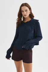 Blusa azul marino de viscosa con cuello a la base, volados en el frente y hombros, cierre frontal con botones y mangas largas con puños fruncidos.