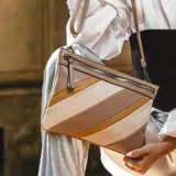 Sobre de mano de símil cuero con diseño de franjas diagonales en negro, blanco y marrón. Cuenta con cierre metálico frontal, bolsillo interior con cierre y otro abierto con división. Incluye correa desmontable para usar como bandolera.