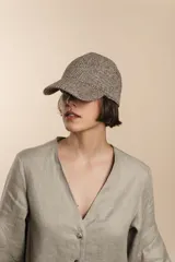 Gorra tipo baseball confeccionada en lana fina sin teñir, con diseño de tejido en espiga en tonos tierra.