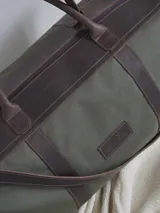 Bolso de lona color verde militar con detalles en cuero marrón. Tiene doble asa de mano y correa de hombro ajustable y extraíble.