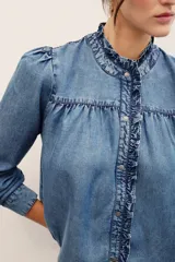 Camisa de denim de lyocell con cierre frontal de broches metálicos, cuello redondo con volados fruncidos y mangas largas con puños doblados.