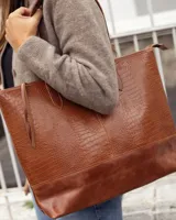 Bolso tipo tote de cuero vacuno, color marrón, con textura efecto reptil en la parte superior y base de cuero liso. Cuenta con doble asa de hombro y cierre superior.