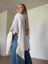 Ruana tejida de algodón con hilo lurex en punto jersey, color azul, con diseño amplio y detalle de etiqueta de cuerina en la parte posterior.