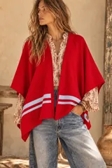Ruana roja de lana con dos líneas horizontales blancas en la parte inferior delantera y detalles de cintas tejidas.