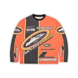 Buzo de manga larga Corteiz con diseño gráfico estilo motocross en colores naranja, negro y amarillo. Presenta múltiples estampados con logotipos y tipografías en el frente y las mangas.