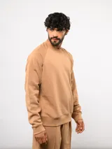 Buzo de cuello redondo color tostado, confeccionado en felpa suave, con diseño de mangas raglán y etiqueta con logo de la marca en el frente.