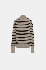 Jersey de punto liso en color beige, con cuello alto y manga larga con detalle de botones metálicos en los puños.