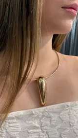 Gargantilla tipo choker rígida de metal dorado con un dije central grande en forma de gota alargada y lisa.