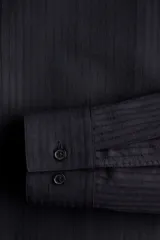 Camisa negra de manga larga con cuello inglés, tapeta clásica, bolsillo superior abierto y canesú con pliegue de caja en la espalda. Los puños tienen cierre ajustable de botón y el bajo es redondeado.