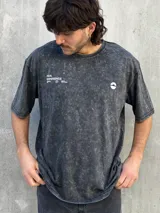 Remera gris con efecto lavado, corte oversize, manga corta y estampado pequeño en el frente.
